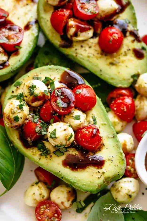 Caprese stuffed avocado halves filled with cherry tomatoes and mozzarella pearls, drizzled with balsamic glaze