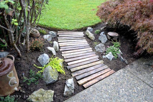 Weathered pallet wood boards laid side by side as a garden walkway, curving between rocks and shrubs