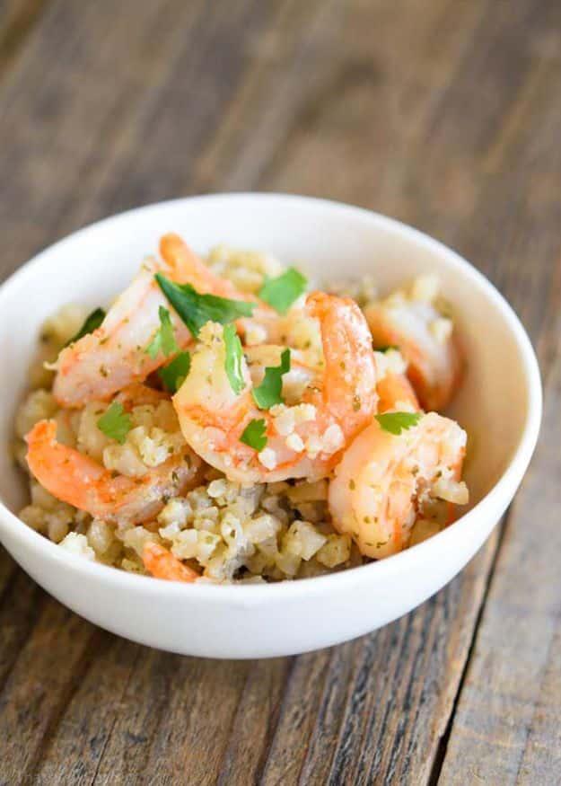 Low carb cauli rice and shrimp in a white bowl on a wooden table, cauliflower rice flecked with pink shrimp