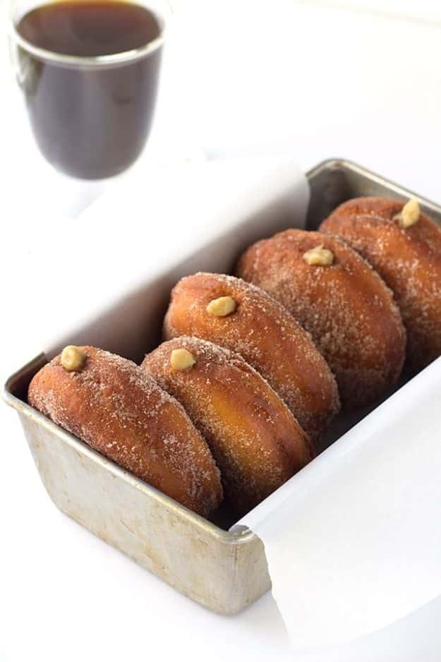 Coffee custard filled donuts rolled in cinnamon sugar lined up in a parchment lined metal loaf pan, mug above