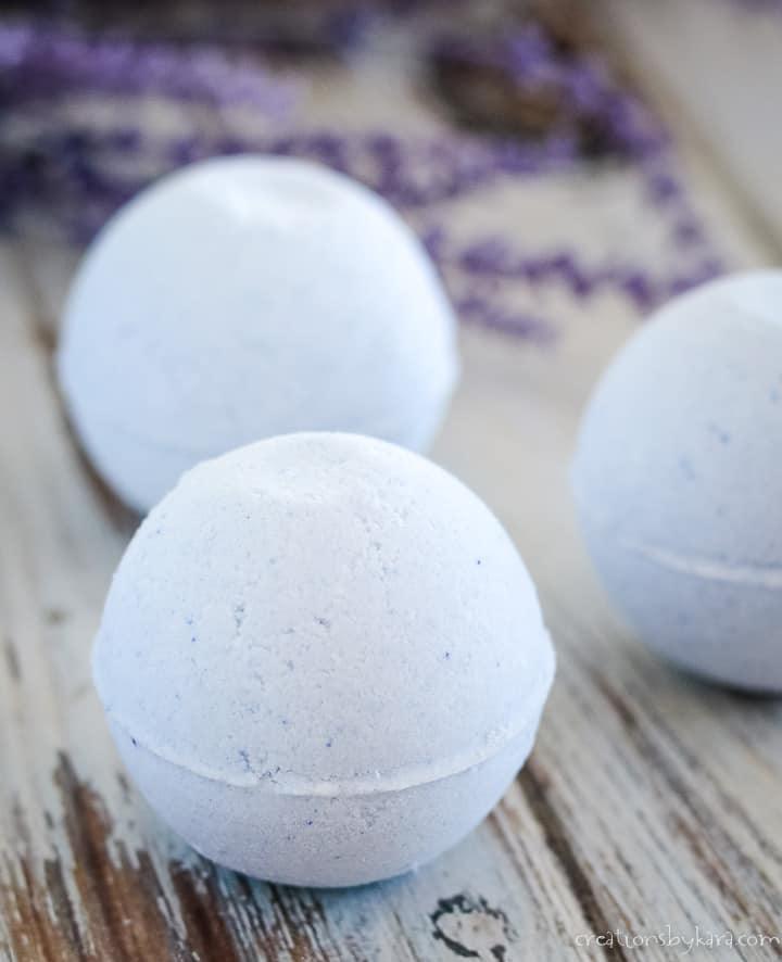 Three pale purple lavender bath bombs on a whitewashed wood board with sprigs of dried lavender behind them