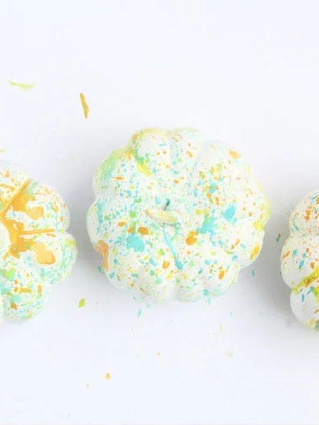 Three small white pumpkins splattered all over with yellow, orange and turquoise paint on a white surface