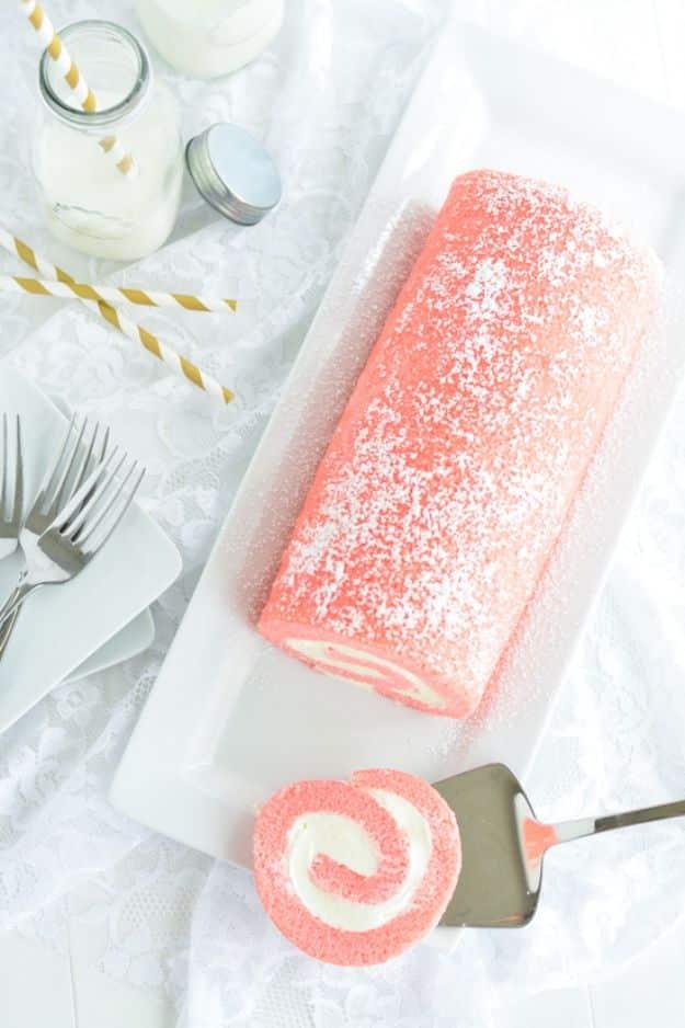 Pink velvet swiss roll dusted with powdered sugar on a white cloth with a cut slice showing the white spiral