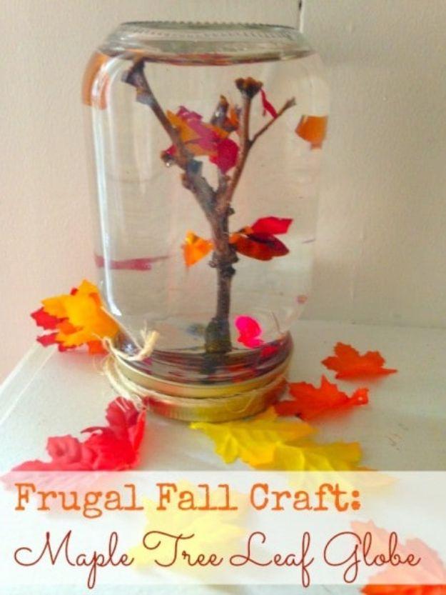 Mason jar snow globe holding water, a bare twig tree and orange confetti leaves, with silk leaves on the lid