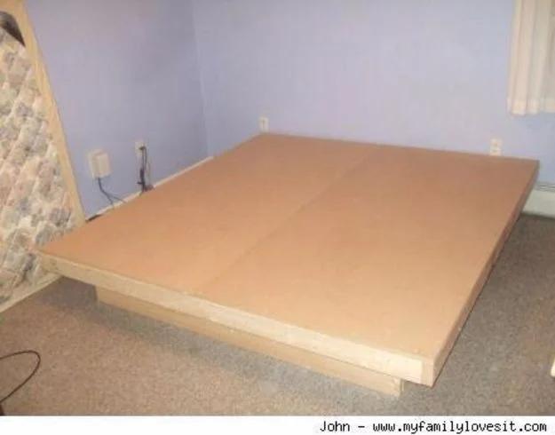 Photograph of a plain low platform bed base made from MDF sheets on a wooden frame in a bedroom with lilac walls