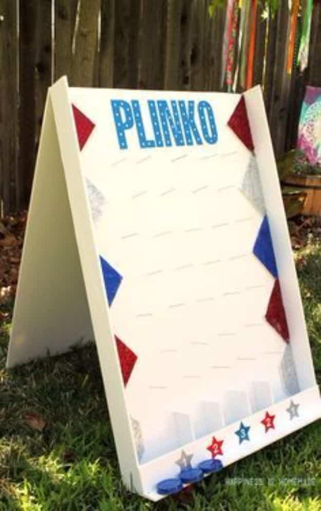 DIY backyard plinko game on a tall white foam board with blue lettering and numbered scoring chutes at the base