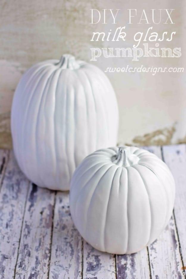 Glossy white faux milk glass pumpkins grouped together on a pale surface with soft neutral fall styling