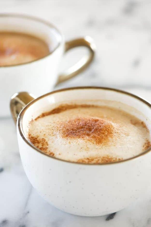 Homemade cinnamon dolce latte in a white mug with cinnamon dusted foam, a second cup behind it on marble