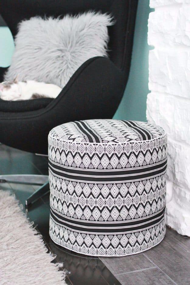 Tall black and white block print drum floor pouf with striped bands top and bottom beside a black egg chair
