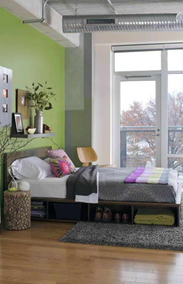 Photograph of a low plywood platform bed with open cubbies and a wide side ledge in a loft bedroom with a green accent wall