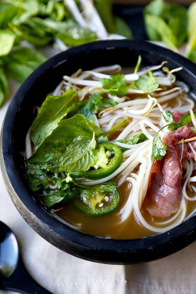 Easy beef pho in a dark stone bowl with rice noodles, raw sliced beef, jalapeno, bean sprouts and herbs