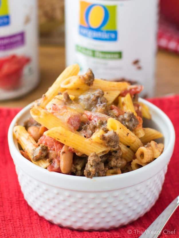 Cheesy chili pasta bake in a white ramekin, penne with ground beef, beans and melted cheese on a red napkin