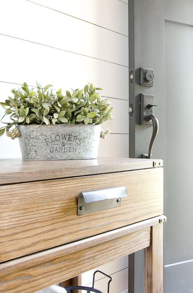 Aged galvanized planter holding faux greenery on a wood console table against white shiplap and a door
