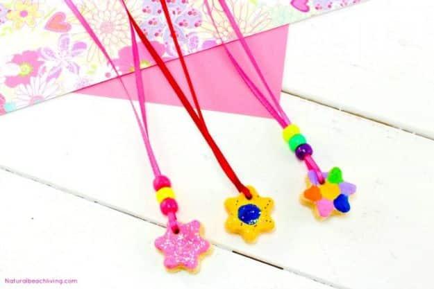 Painted salt dough star and flower pendants strung on red cord with beads, laid on a white wood table
