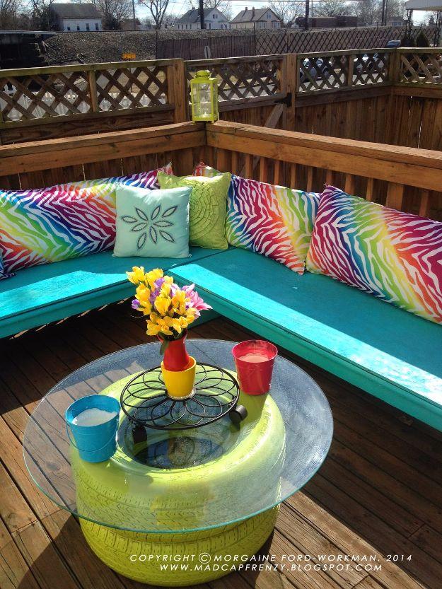Three lime green painted tires stacked as a deck table base under a round glass top beside bright striped cushions