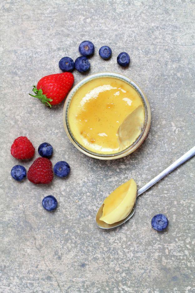 Small glass jar of pale yellow vegan creme brulee on grey stone with fresh berries and a spoonful beside it