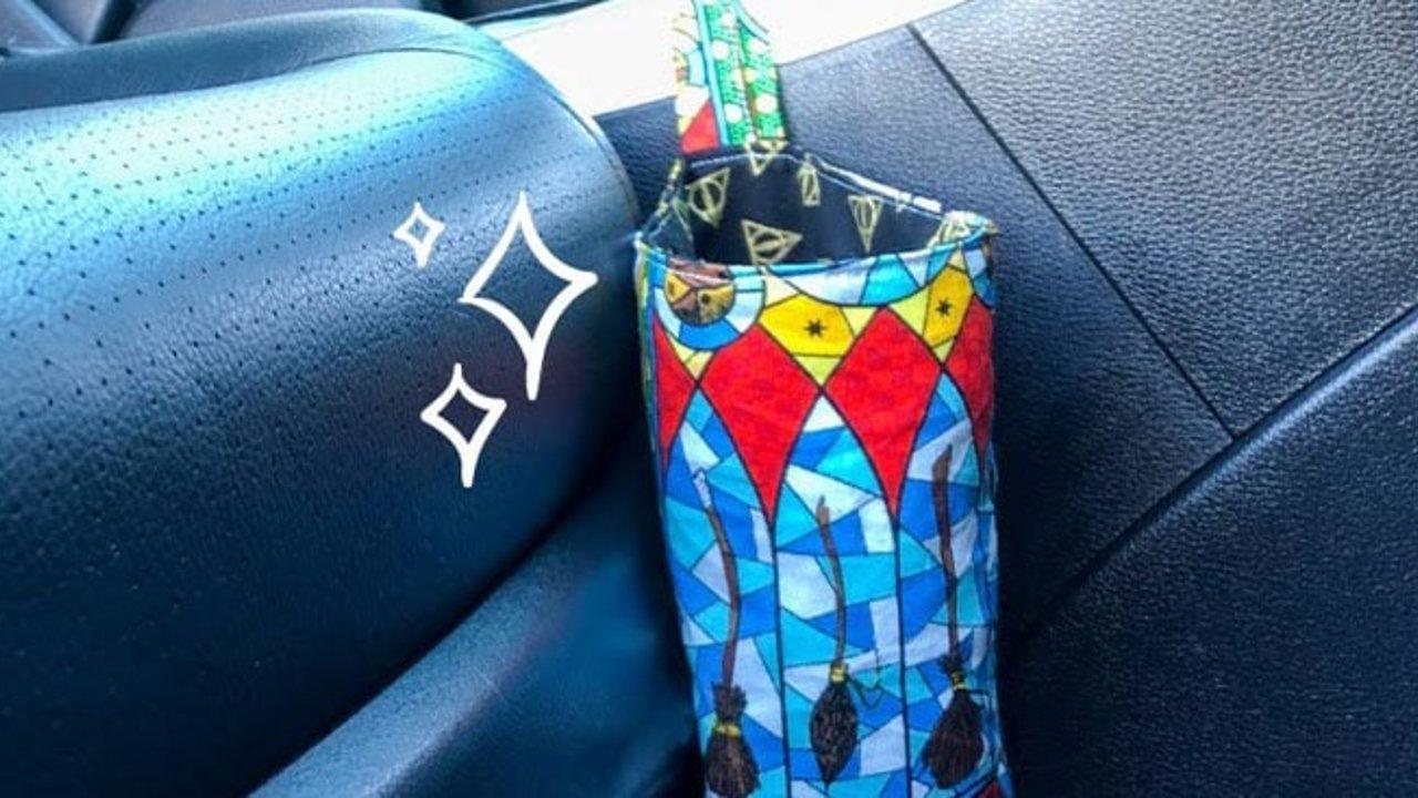 Car trash can sewn from bright stained glass print cotton, hanging by its strap from a black leather car seat