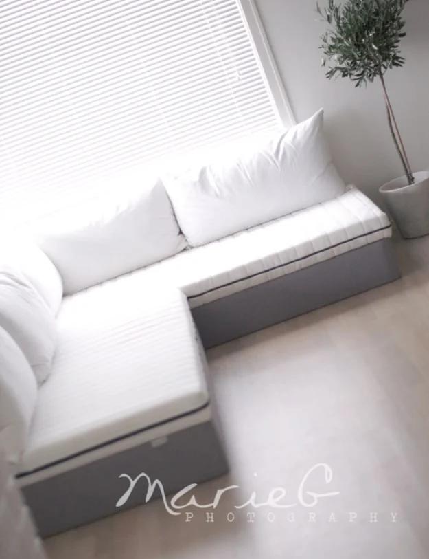 White L shaped sofa built from cut down bed frames with white seat and back cushions in a bright room by a window