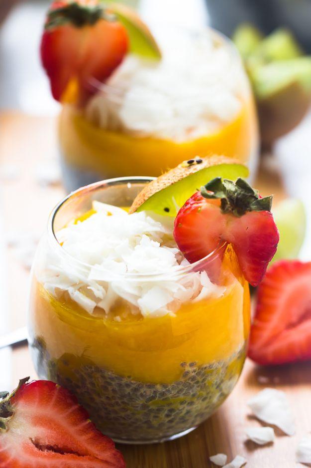 Layered mango coconut chia pudding in a tall glass topped with cream, a strawberry and a slice of kiwi