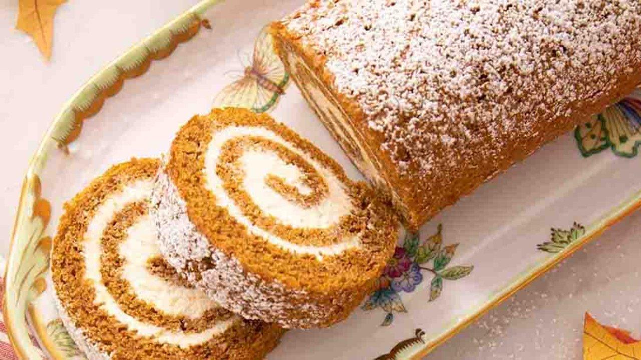 Pumpkin cake roll on a floral platter, two spiral slices cut showing the cream cheese filling inside