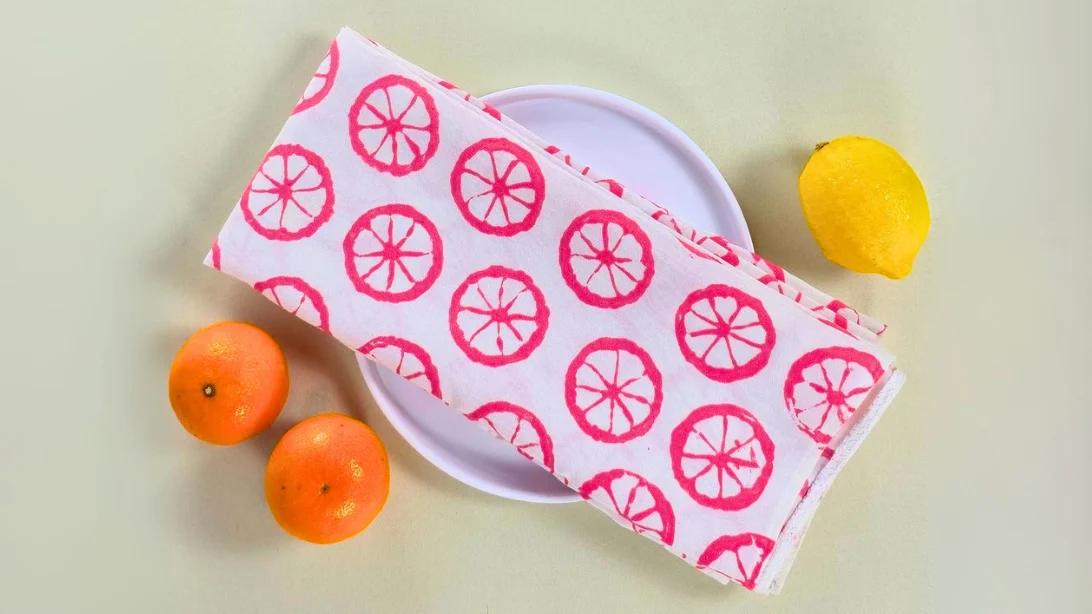 A flour sack towel printed with yellow lemon halves in fabric paint, folded on a bright kitchen counter