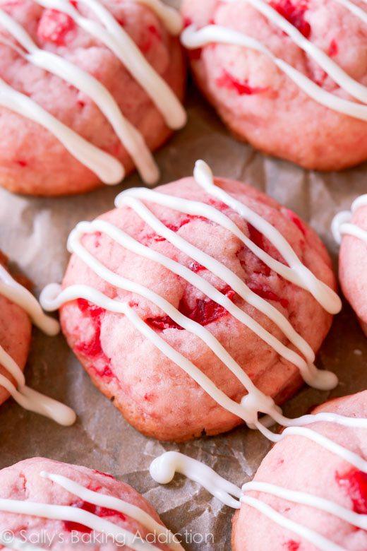 Pink cherry almond shortbread cookies flecked with maraschino cherries and drizzled with white chocolate on parchment