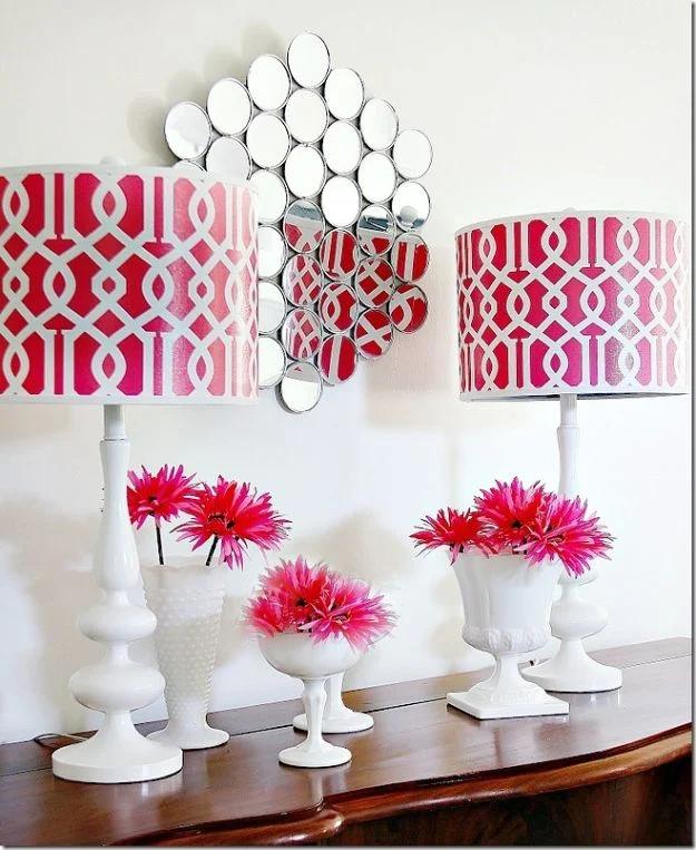 Wall mirror made from painted dollar store compacts arranged above a console with pink lamps and flowers