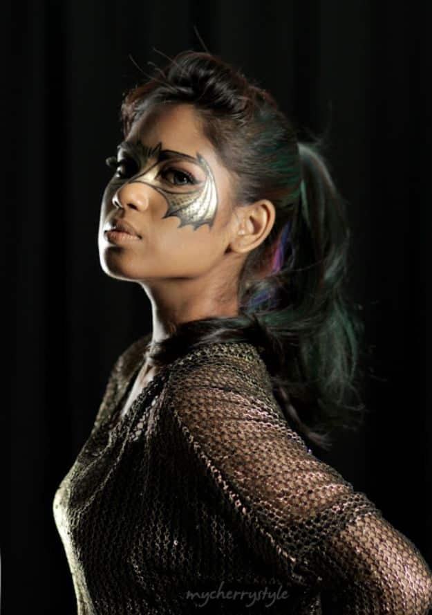 Bat eye Halloween makeup with metallic gold paint, black wing shapes across the eyes and a dark mesh top