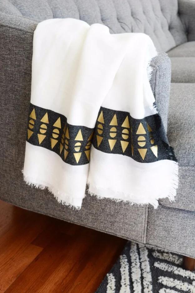 White fringed throw folded over a gray sofa, a black band of gold geometric shapes running across each end