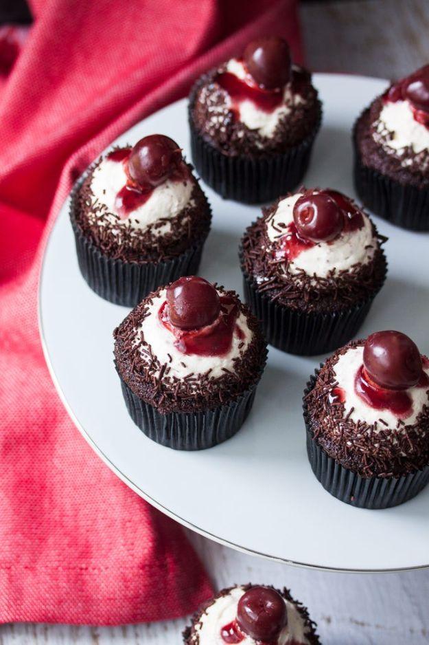 Black forest chocolate cupcakes topped with cream, a cherry and chocolate shavings on a plate over red cloth