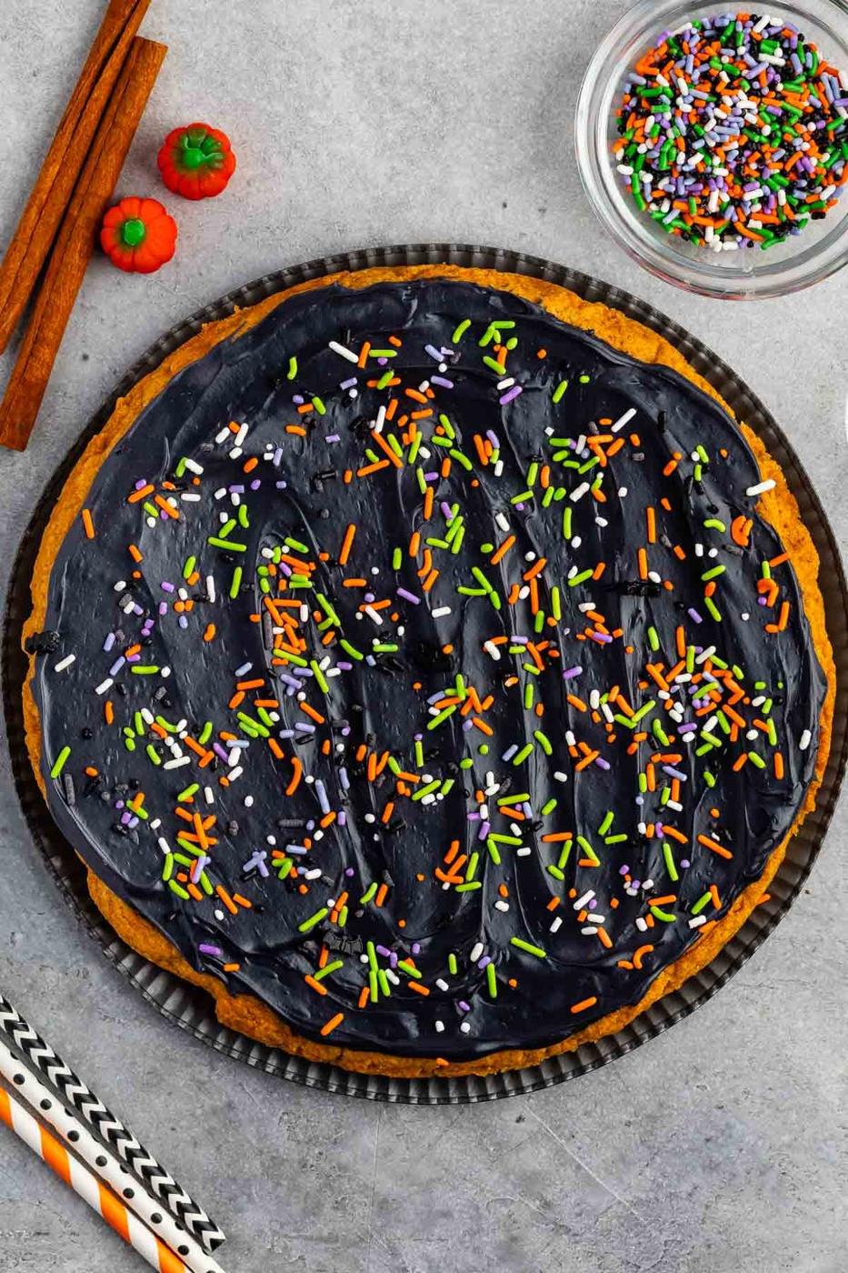 Large round pumpkin cookie cake frosted black and covered with orange white and purple Halloween sprinkles