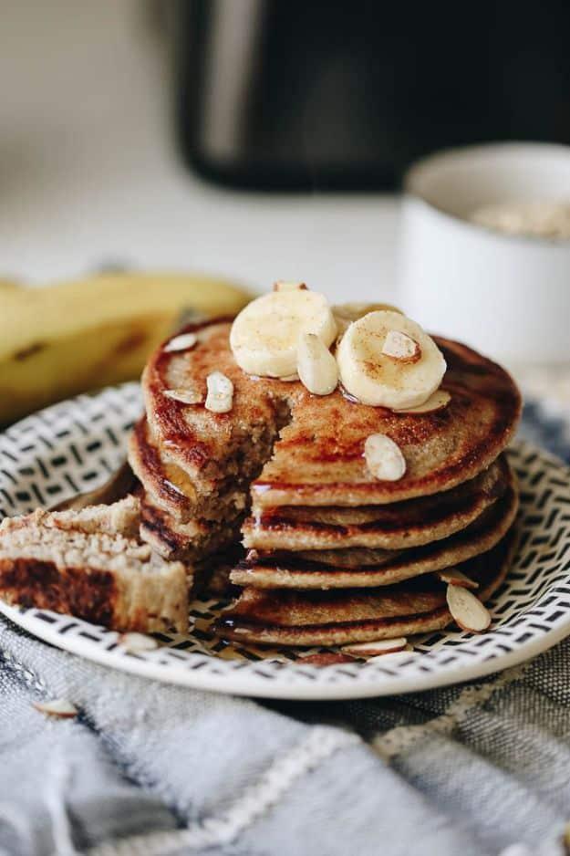 Banana oatmeal blender pancakes on a white lattice edged plate with a wedge cut out, banana slices and almonds