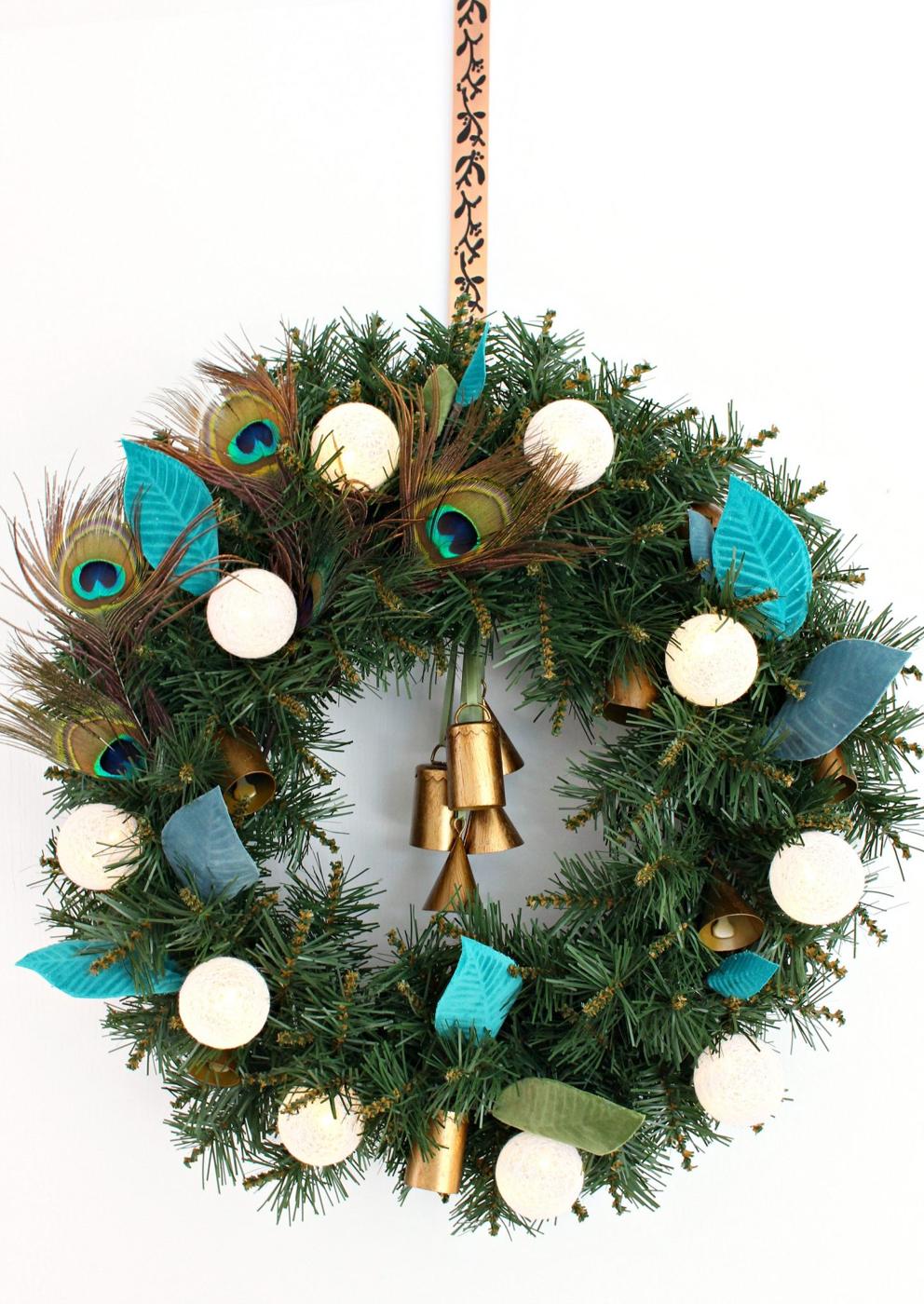 Evergreen wreath trimmed with peacock feathers and teal and gold ornaments, a boho wreath for a door