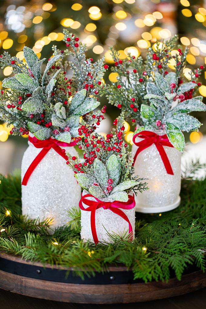 Three mason jars frosted with Epsom salt and glitter, filled with evergreen and tied with red velvet ribbon in a wooden tray