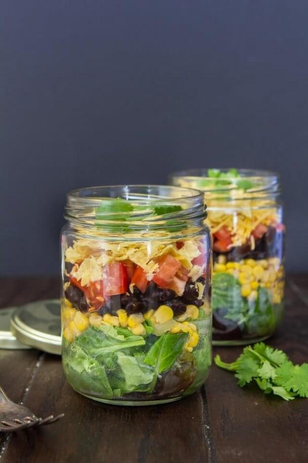Mexican salad in a jar with beans, corn, cheddar and crushed tortilla chips layered under fresh lettuce