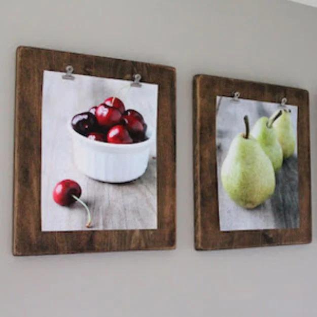 Three wooden clipboards painted in soft blush and gray, hung in a row on a white wall holding swapped out family photos