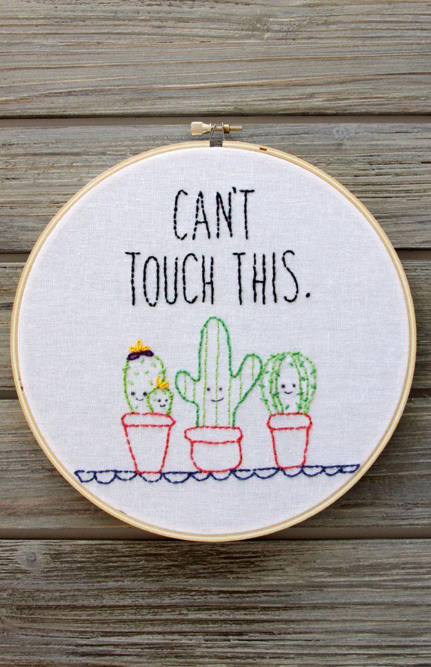 Wooden hoop on gray barn boards holding white linen stitched with smiling cacti in three pots under block lettering