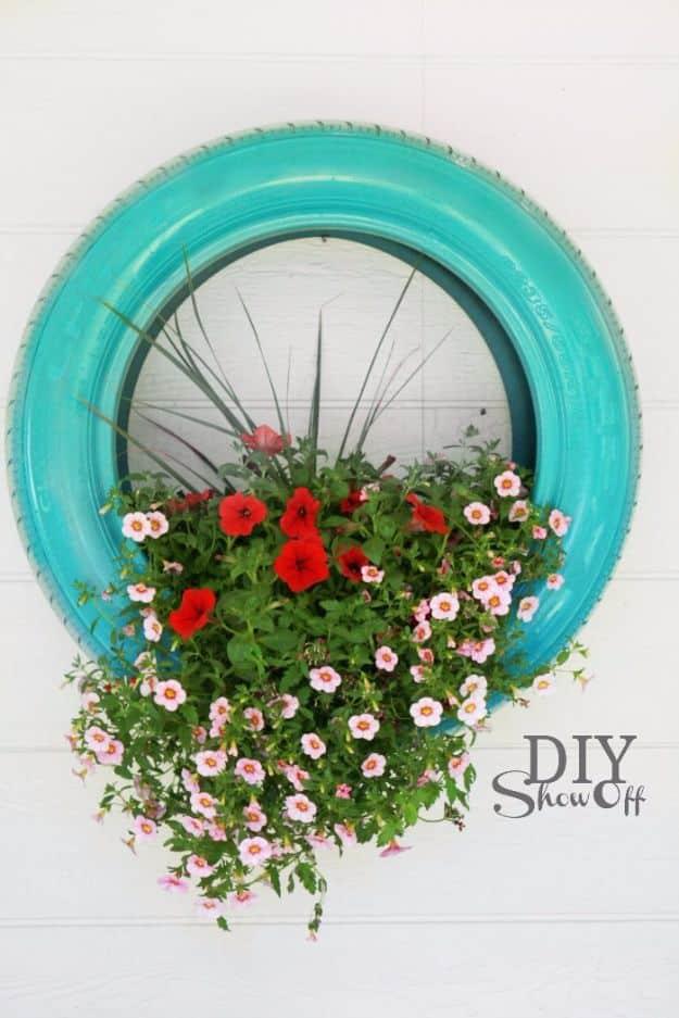 Teal painted old tire planter hung on white siding with red and pink petunias spilling out of the front