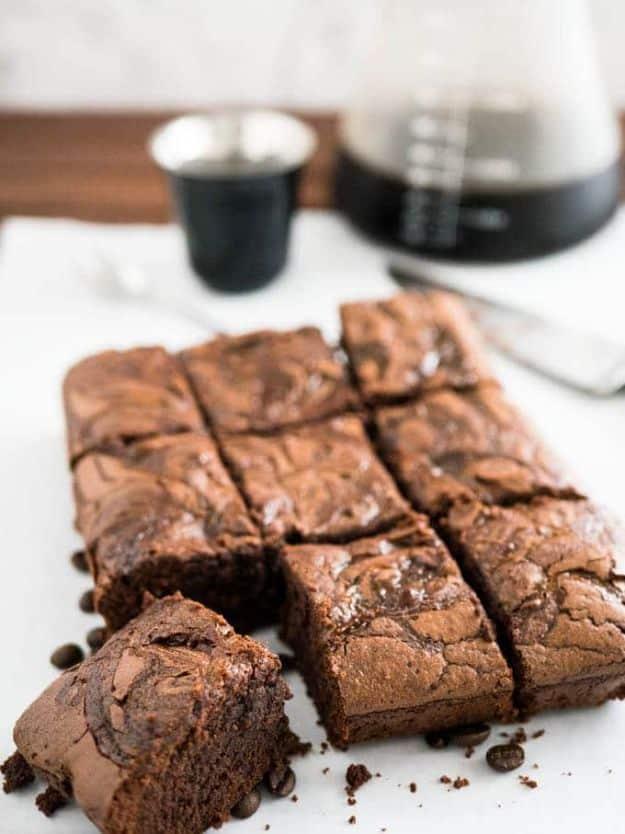 Cold brew coffee brownies cut into nine squares with crackly tops on a board, a coffee pot and cup behind