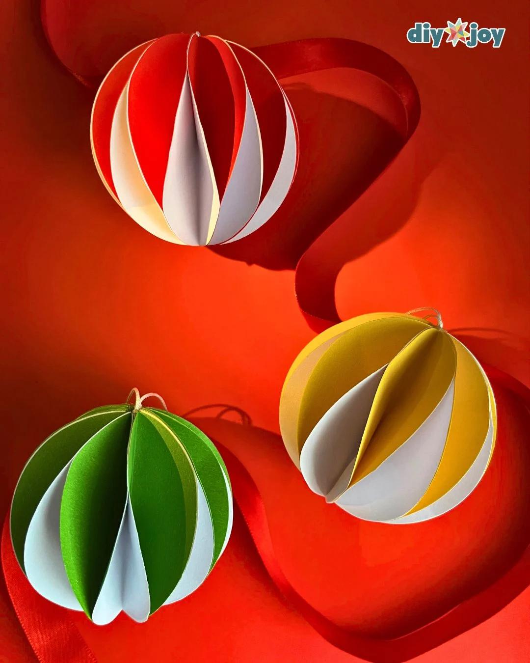 DIY Ideas - three finished paper ball ornaments in red and white, yellow and white, and green and white on a red ribbon background
