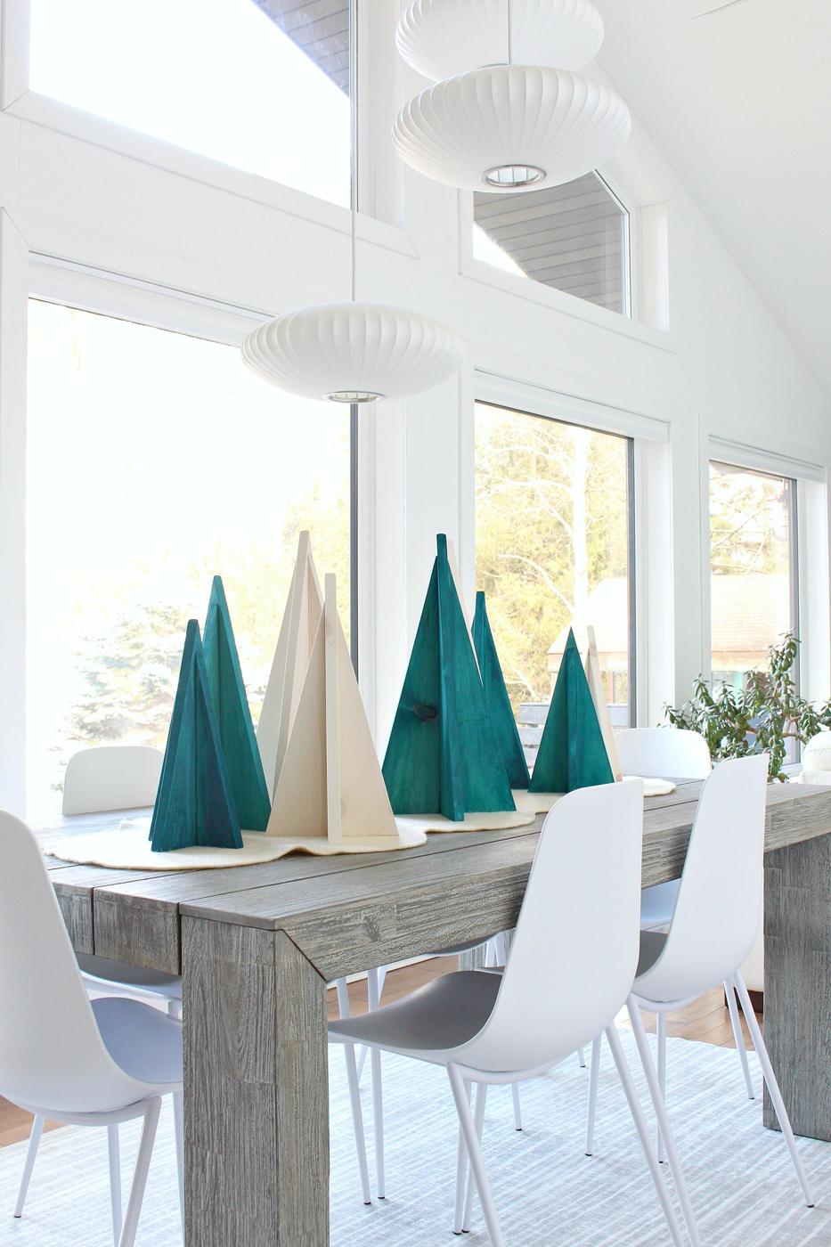 Six wooden triangle Christmas trees in turquoise stain and natural pine on a cream felt runner on a gray dining table