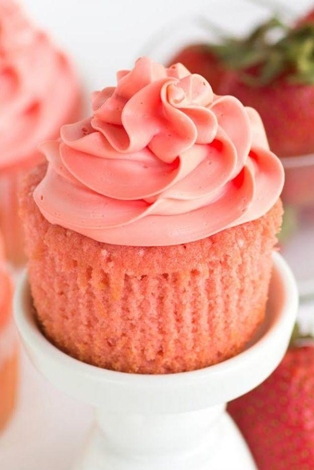 Pink strawberry cupcake with a tall swirl of pink frosting on a white cake stand beside fresh strawberries