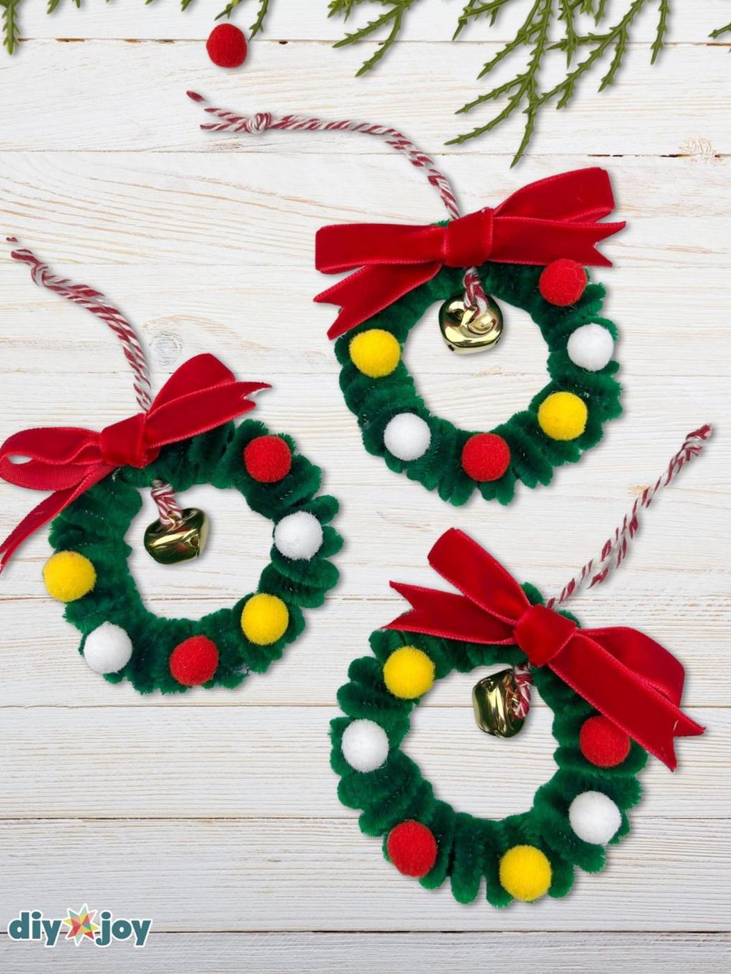 Three mini wreath ornaments made of green pipe cleaners with red, white and yellow pom poms, gold bells and red velvet bows