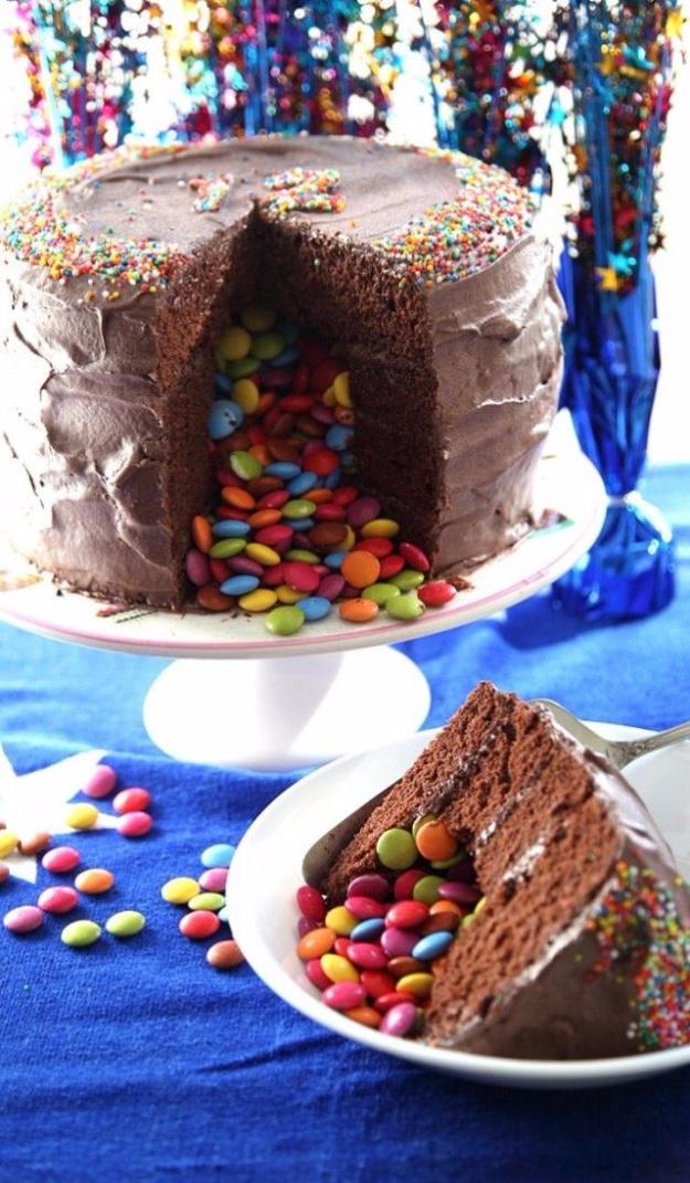 Chocolate pinata birthday cake cut open with colored candies spilling out of the hollow center onto a stand