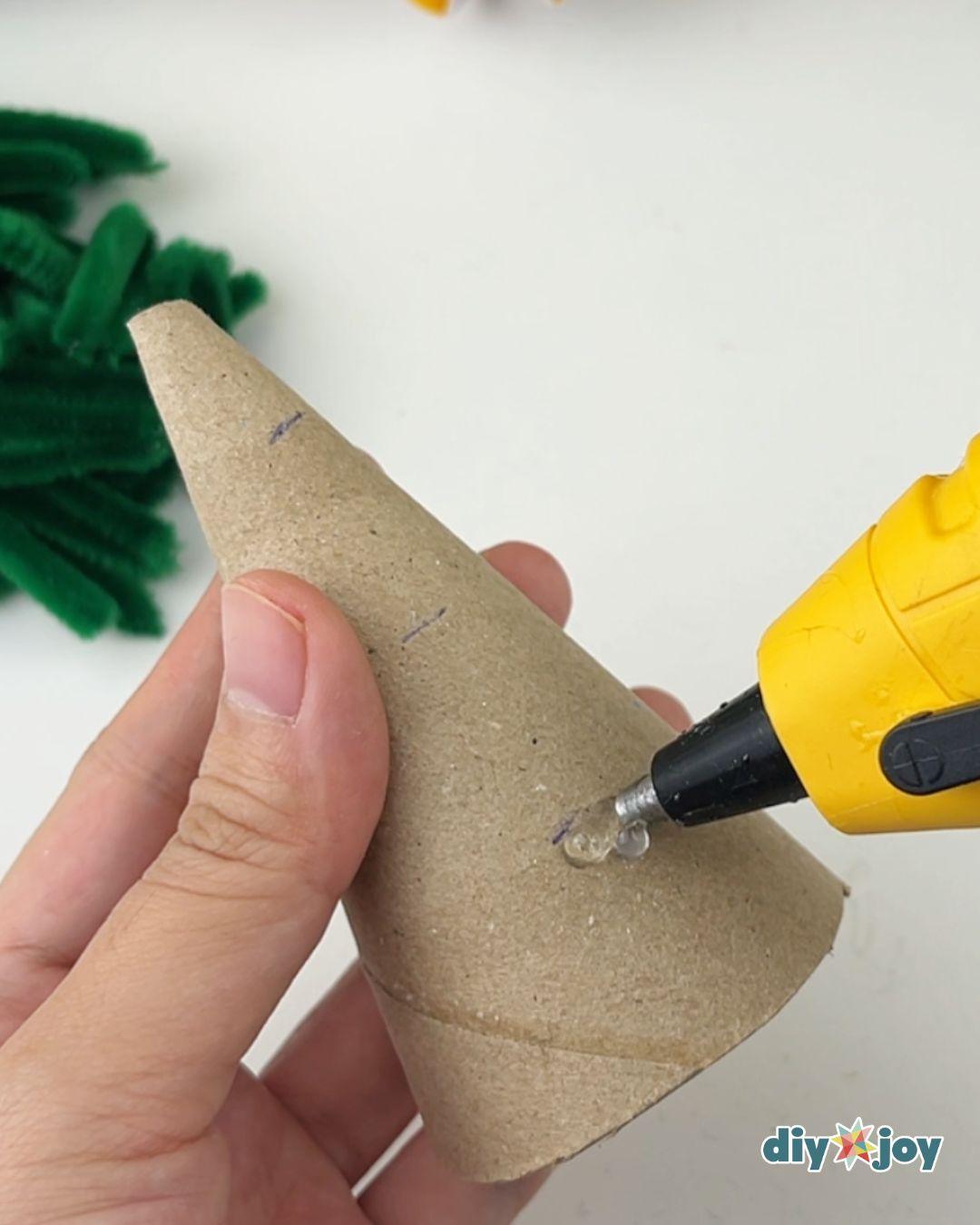 How to Make a Christmas Tree - a hand steadies a pencil marked cardboard cone while a glue gun lays a bead of hot glue along one mark