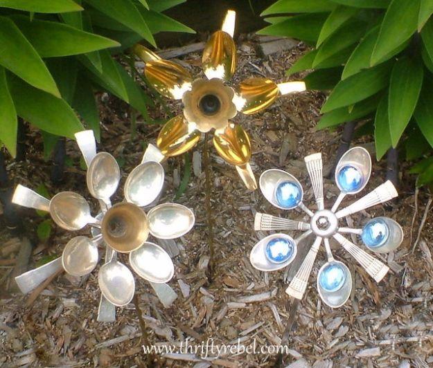 Three garden flowers made from spoon and fork bowls fanned around a centre, staked in a mulched garden bed