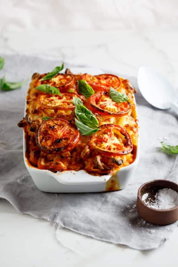 Caprese mac and cheese layered in a white baking dish with roasted tomato slices and torn fresh basil leaves
