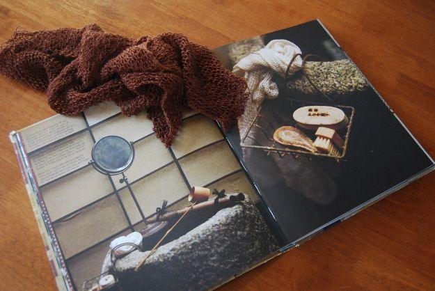 Open book showing Japanese bath scenes on a wooden table with a loosely knit brown washcloth draped over the left page