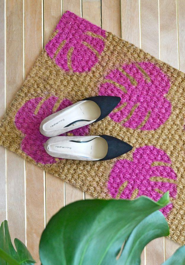DIY leaf doormat, a coir doormat stencilled with large hot pink monstera leaves, lying on a wooden deck outside
