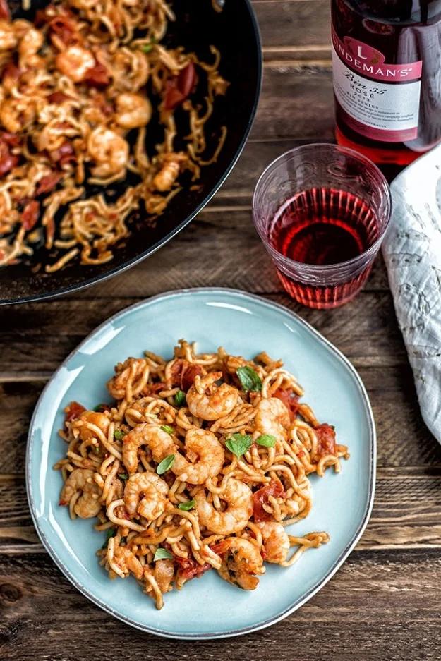 Chili prawn noodles in a wok with king prawns, cherry tomatoes and fresh Thai basil leaves over egg noodles